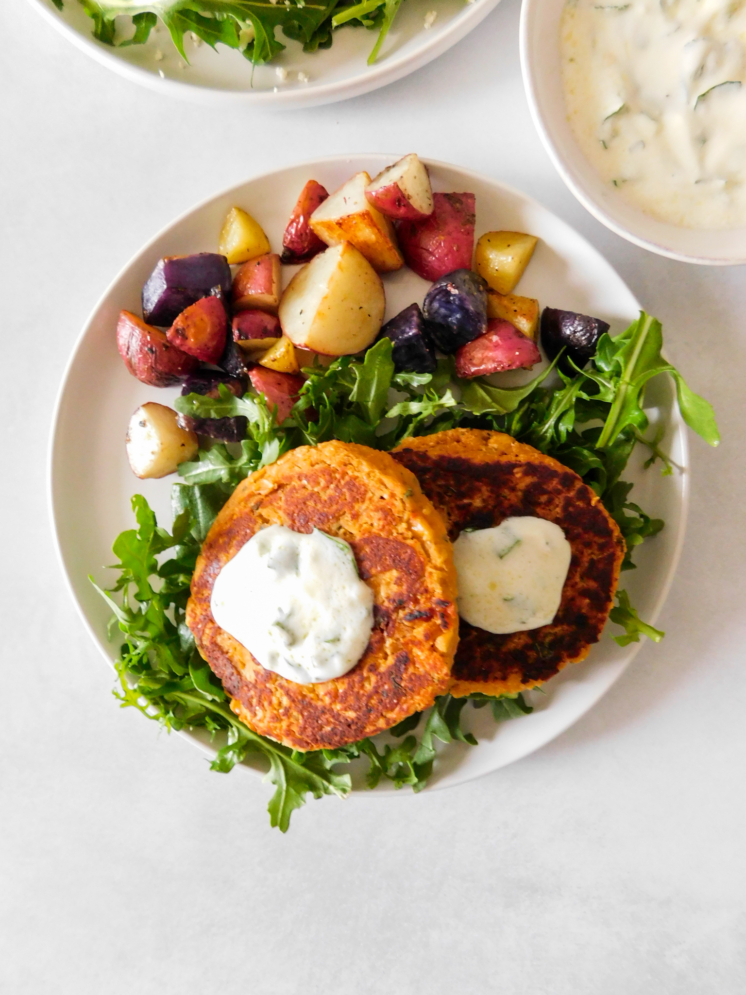 An overhead view of two chickpea patties on a plate with arugula and roasted potatoes. 