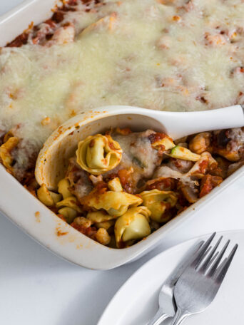 Cheesy tortellini casserole in a baking dish with a serving spoon.