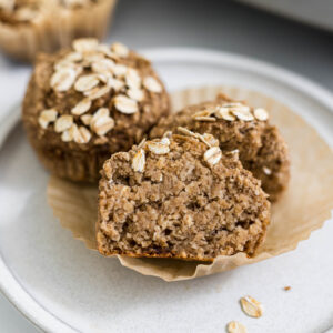 A Banana Applesauce Muffin cut in half resting on another muffin on a plate.