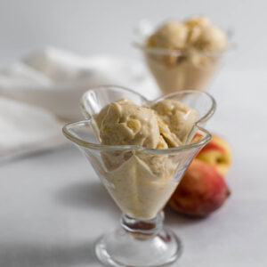 Two glasses with nectarine nice cream in them and some nectarines in the background.