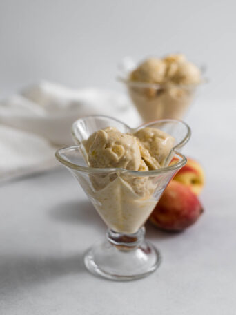 Two glasses with nectarine nice cream in them and some nectarines in the background.