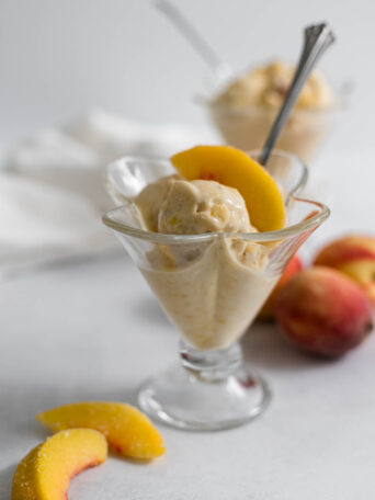 Peach nice cream in an ice cream glass with a peach on top.