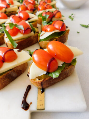 A close up of Avocado Caprese Crostini with more crostini in the background. They're sitting on a white marble serving board.