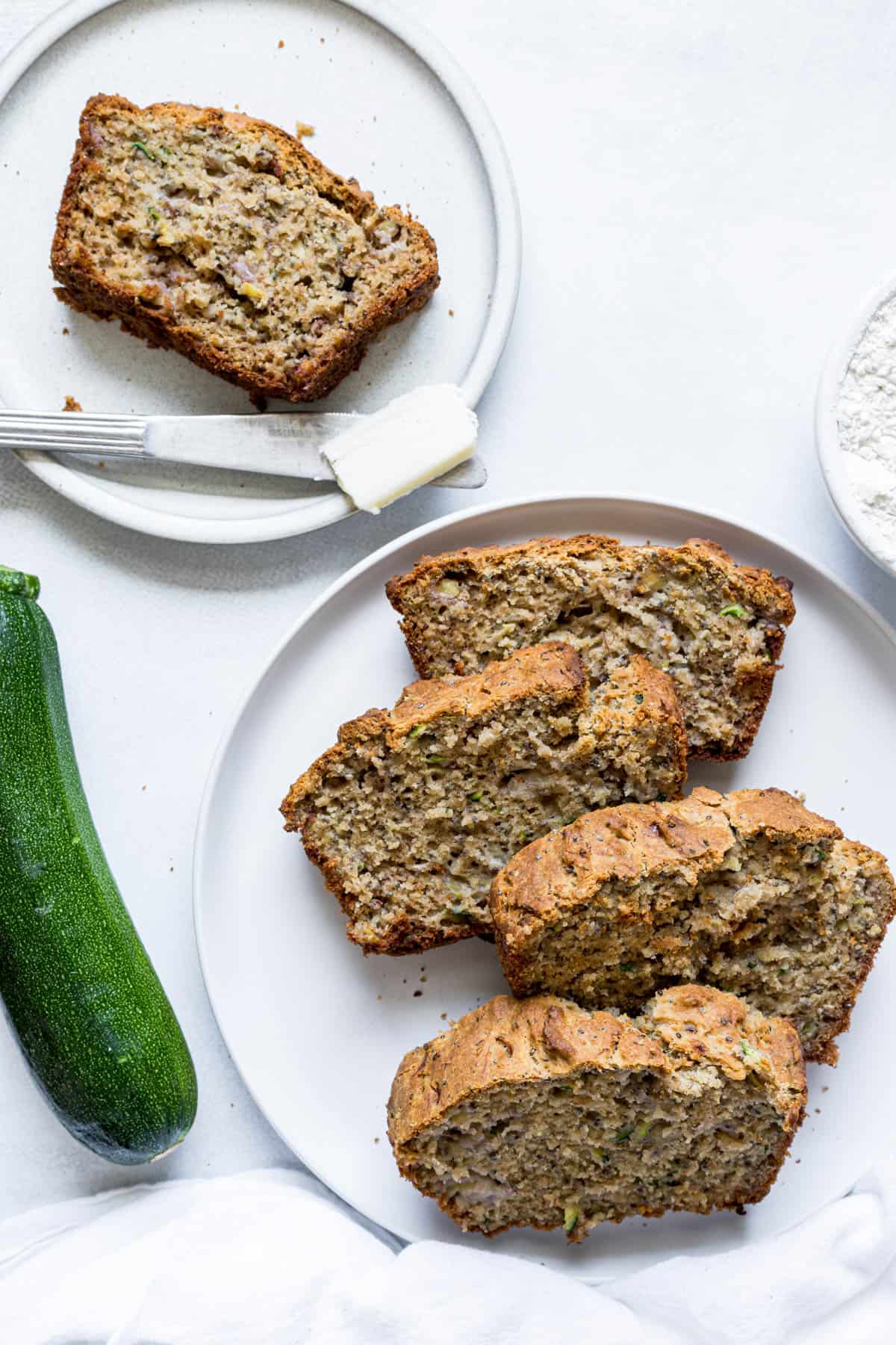 Slices of banana bread on two plates. A knife with butter sits on one of the plates.