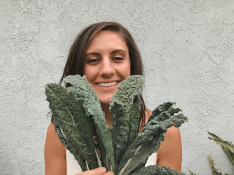 Kaileigh is smiling behind a bunch of kale leaves.