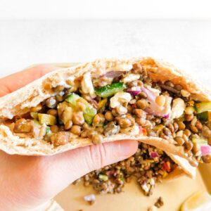 A white hand is holding a mediterranean lentil pita pocket.