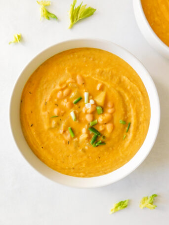 A bowl of Creamy Vegan White Bean Potato Soup with a celery leaves surrounding it.