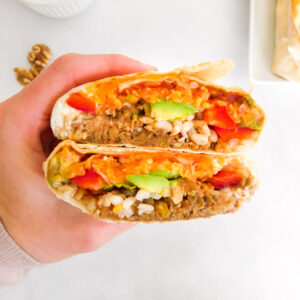 A hand is holding a lentil walnut burrito that is cut in half.