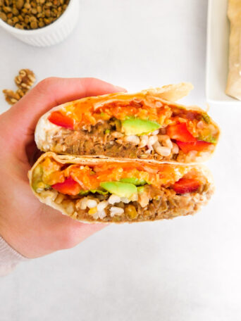 A hand is holding a lentil walnut burrito that is cut in half.