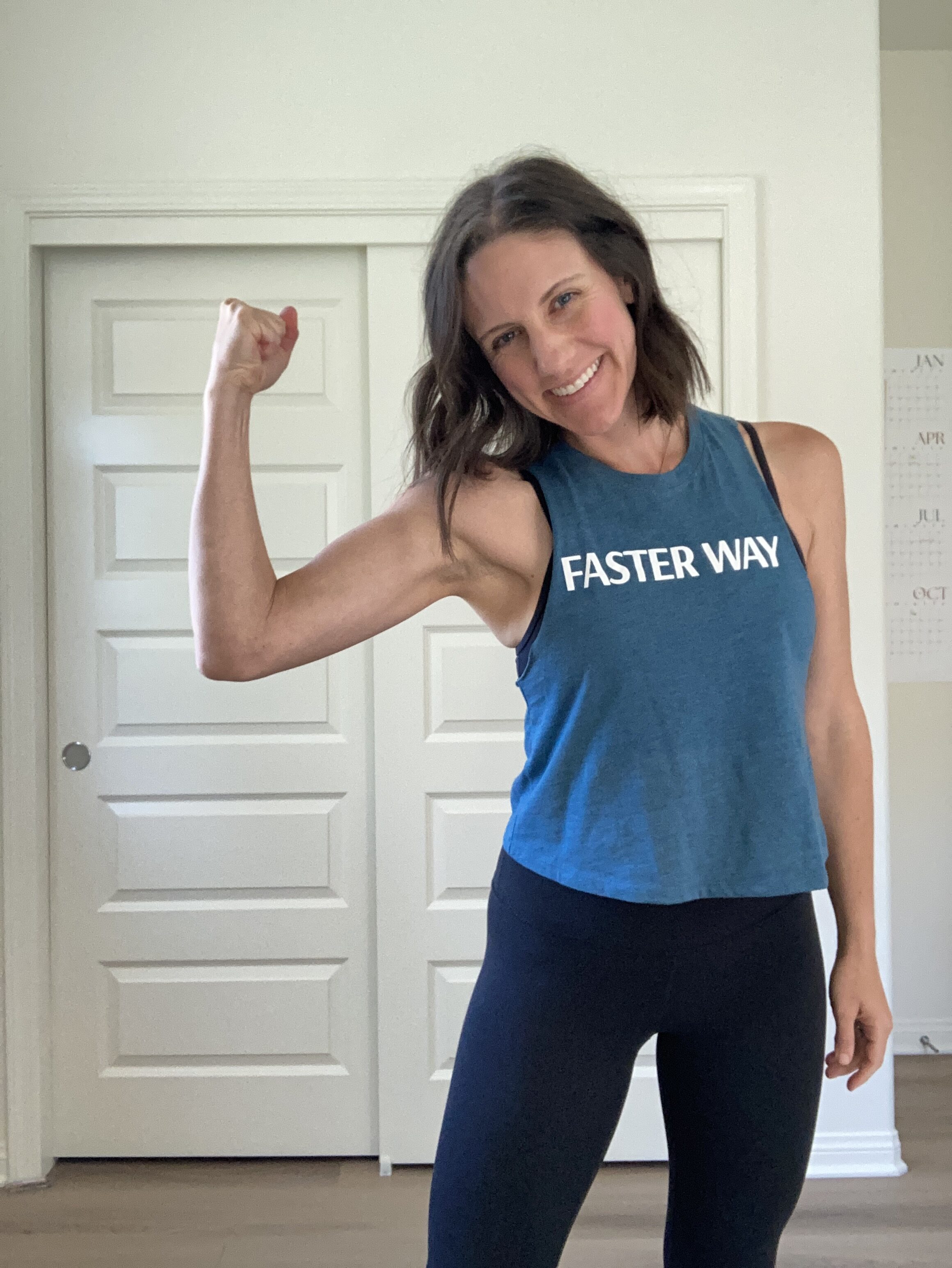 Kaileigh flexing her arm and smiling, wearing a FASTer Way shirt.