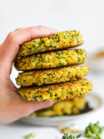 A hand holding a stack of Cheesy Broccoli Quinoa Patties.