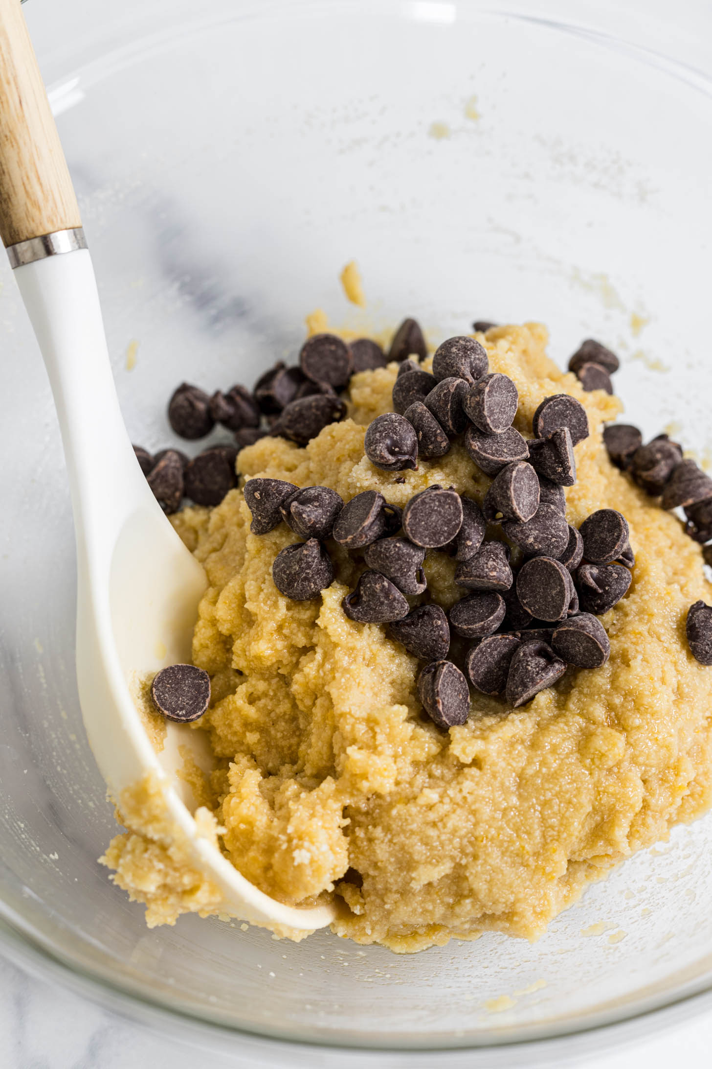 Cookie dough with chocolate chips in a mixing bowl with a spoon.