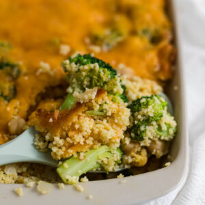 A spoon scooping out the couscous casserole with a piece of broccoli in it.