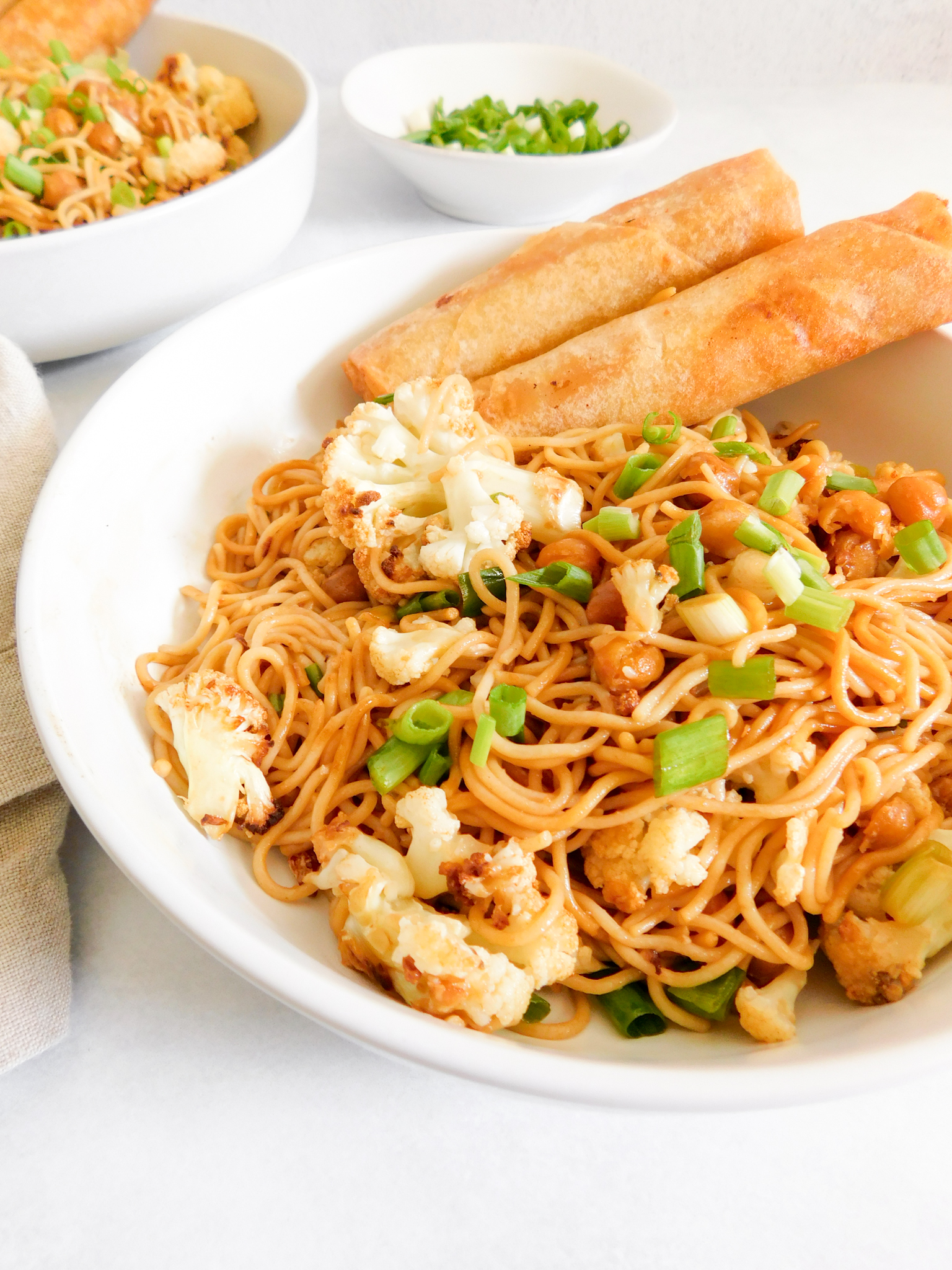 A bowl of ramen noodles with veggies in them and two spring rolls in the bowl. 