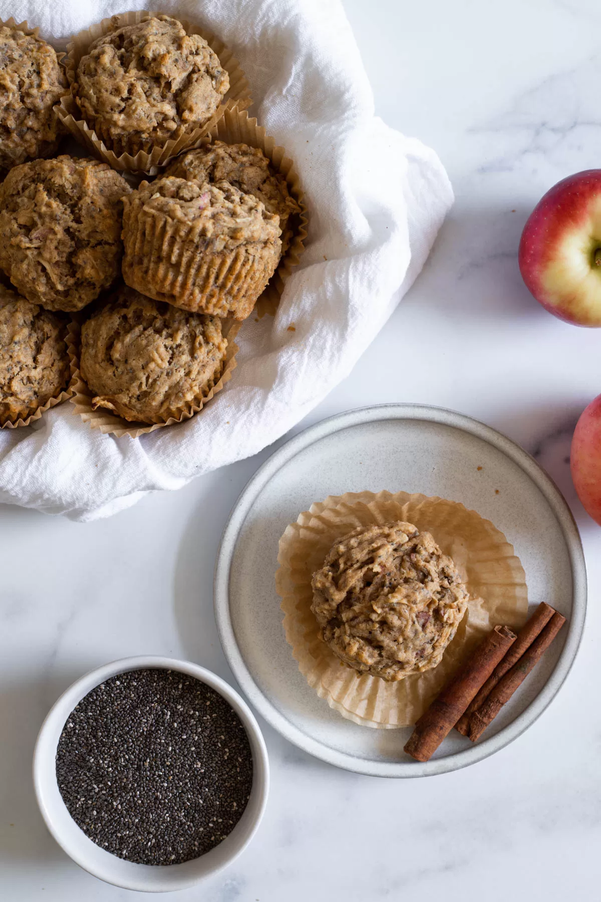 Apple muffin on a plate next to a bowl of muffins.