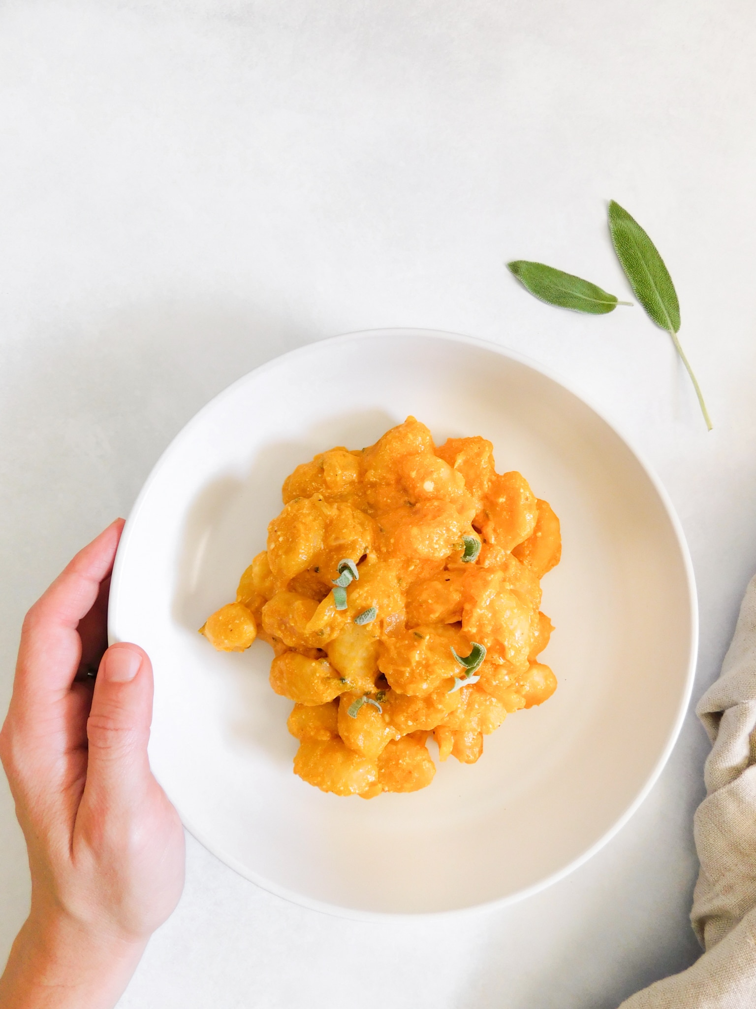 Kaileigh's left hand is resting on the side of a bowl of pumpkin gnocchi.