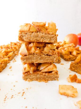 A stack of Easy Apple Pie Bars with more bars surrounding it and two apples in the background.