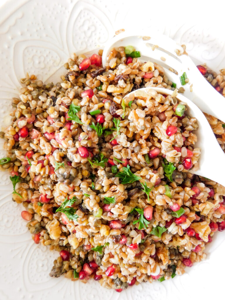 A close up image of the farro lentil salad with two serving spoons sitting in the bowl.