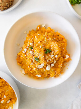 A bowl of roasted butternut squash risotto with feta crumbles sprinkled on top and some parsley leaves.