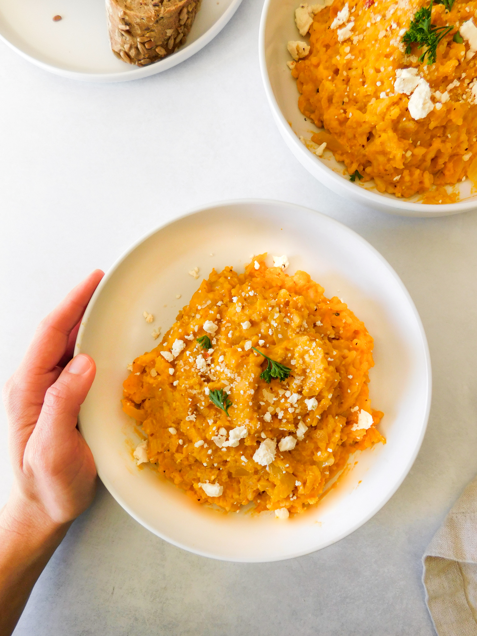 A hand is placed around a butternut squash risotto bowl.