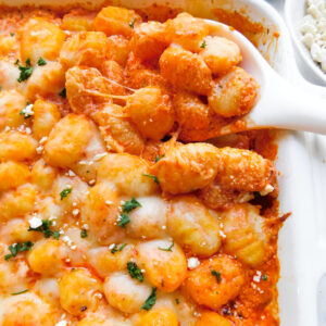 A close up view of feta baked gnocchi with a serving spoon scooping some out.