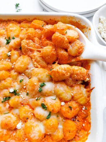 A close up view of feta baked gnocchi with a serving spoon scooping some out.