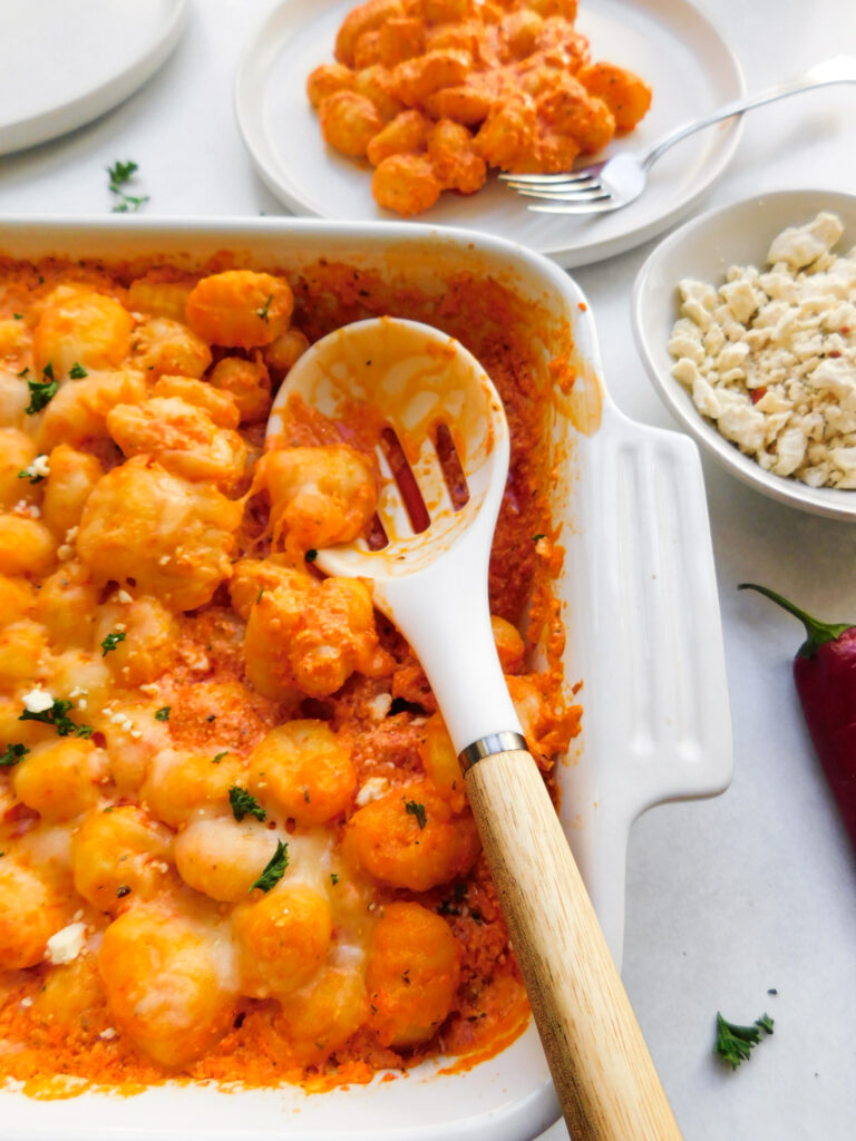 A baking dish with the Feta Gnocchi Bake and a plate of gnocchi in the background. 