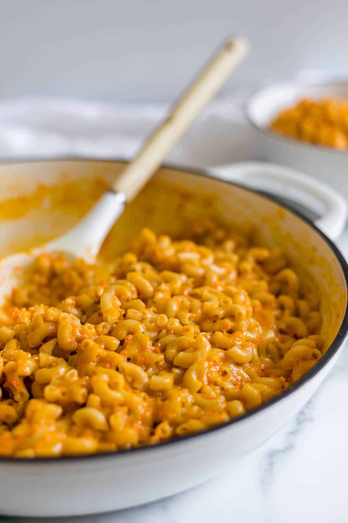 A side view of mac and cheese in a big serving dish with a serving spoon in it.