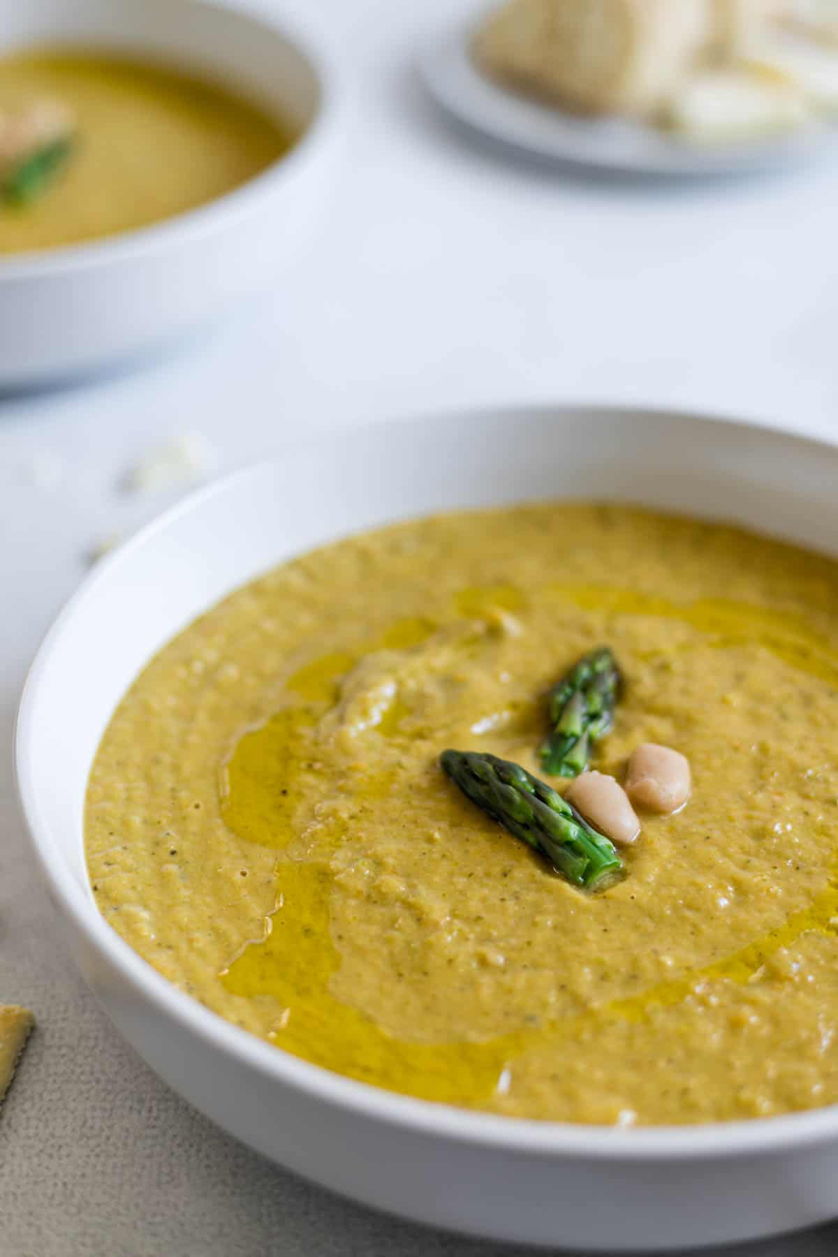 A bowl of asparagus soup with two asparagus tips and white beans in the center of the soup.