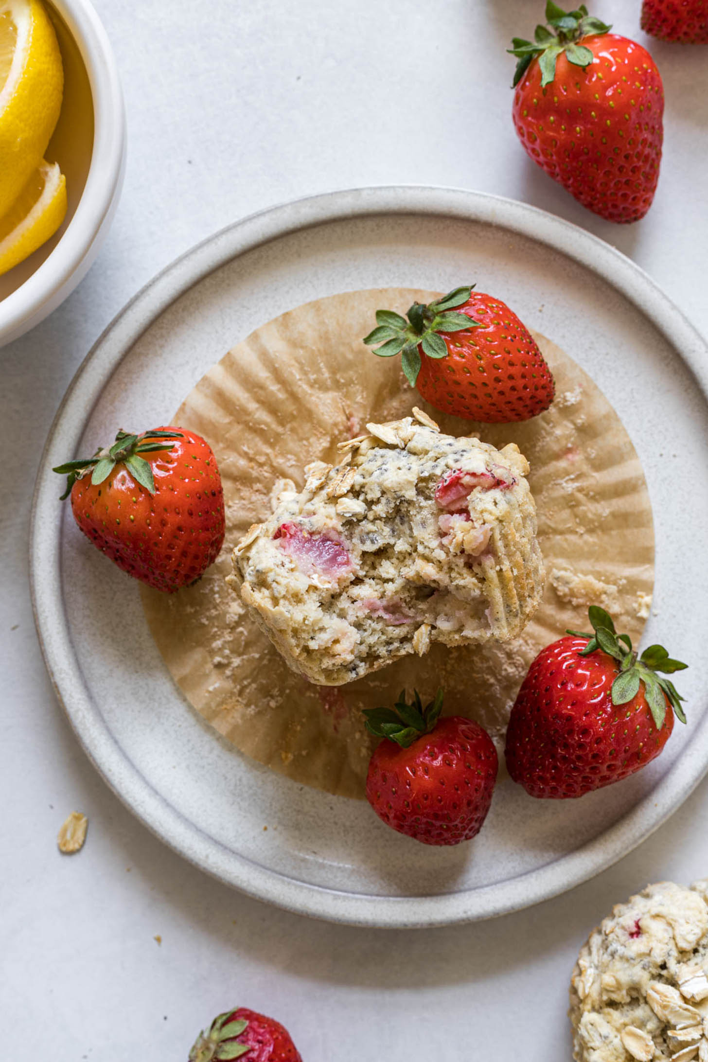 A strawberry muffin with a bite out of it with strawberries around it.