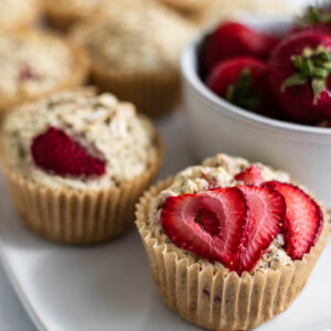 Vegan Strawberry Muffins on a plate next to a bowl of strawberries.