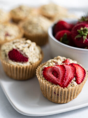 Vegan Strawberry Muffins on a plate next to a bowl of strawberries.