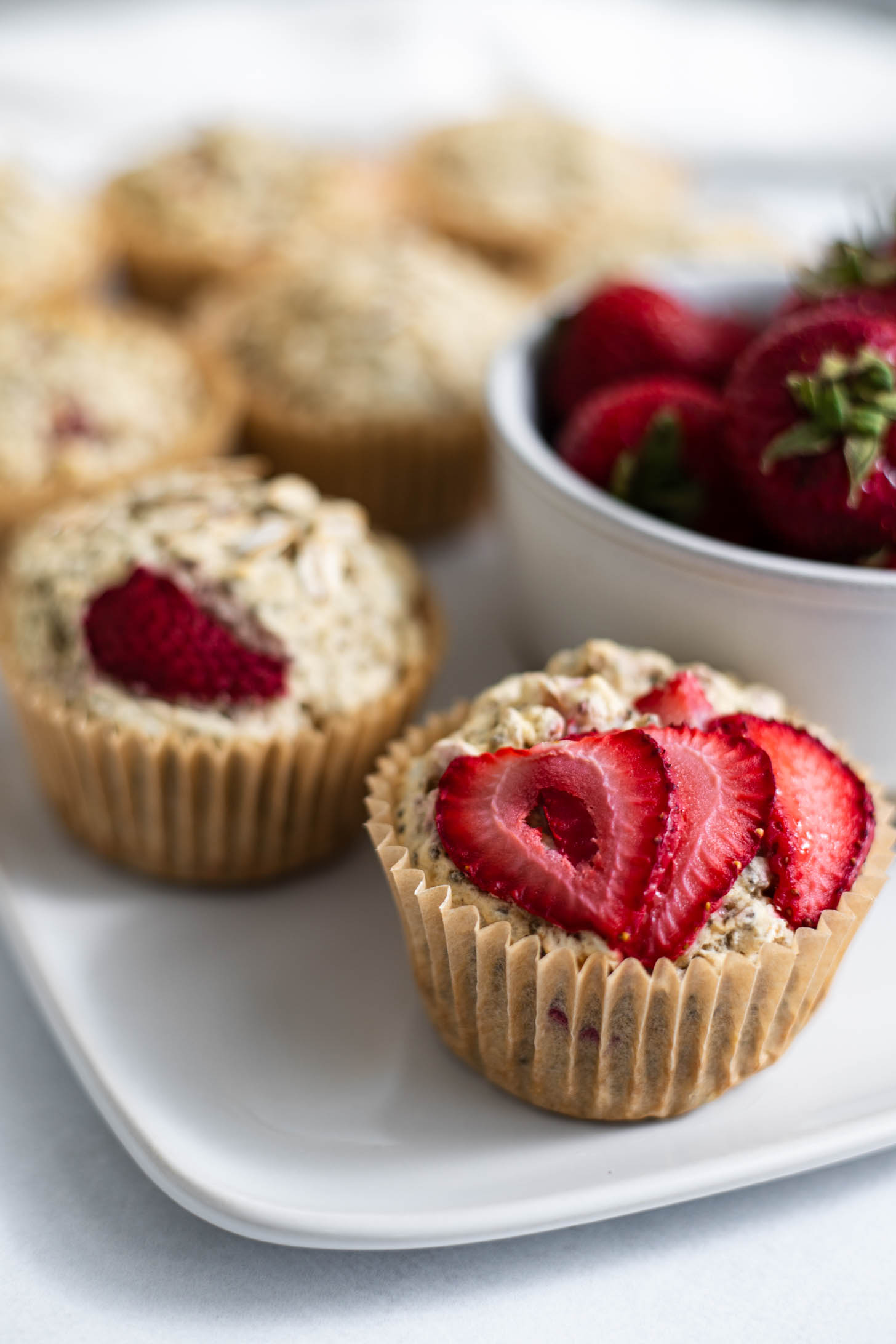 Vegan Strawberry Muffins on a plate next to a bowl of strawberries.