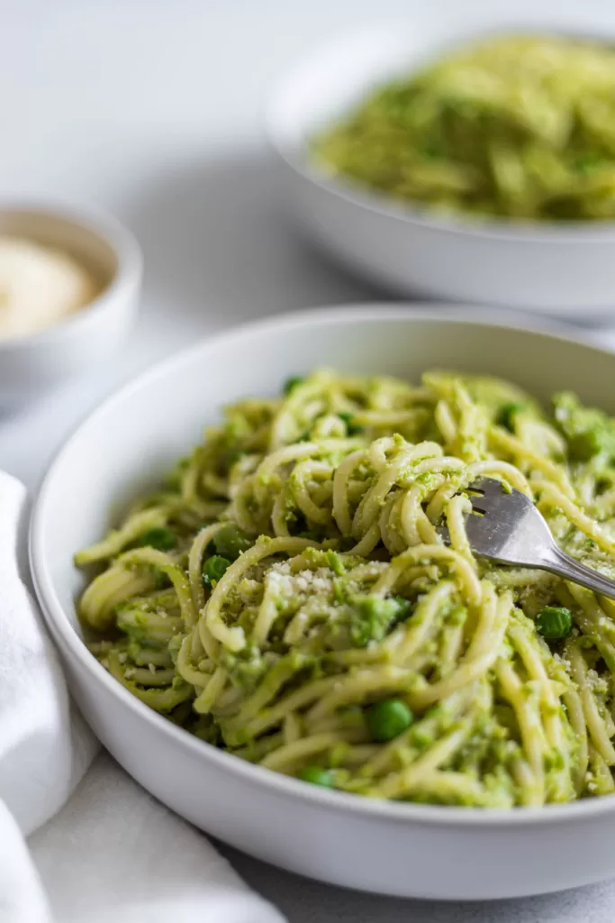 A close up view of a side view bowl of pasta with a fork in it. Another bowl of pasta is behind it.