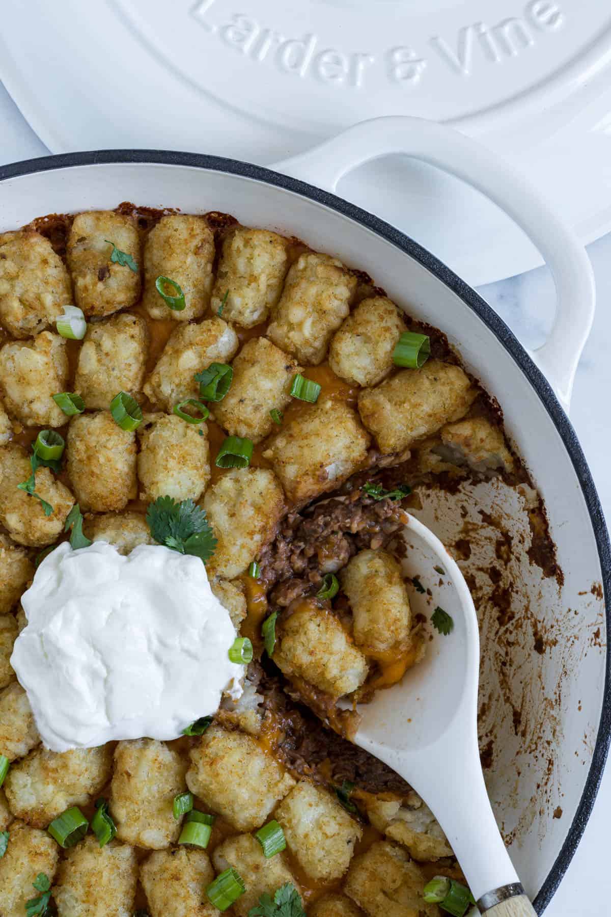 A close up view of a serving spoon resting in the tater tot casserole braiser dish.