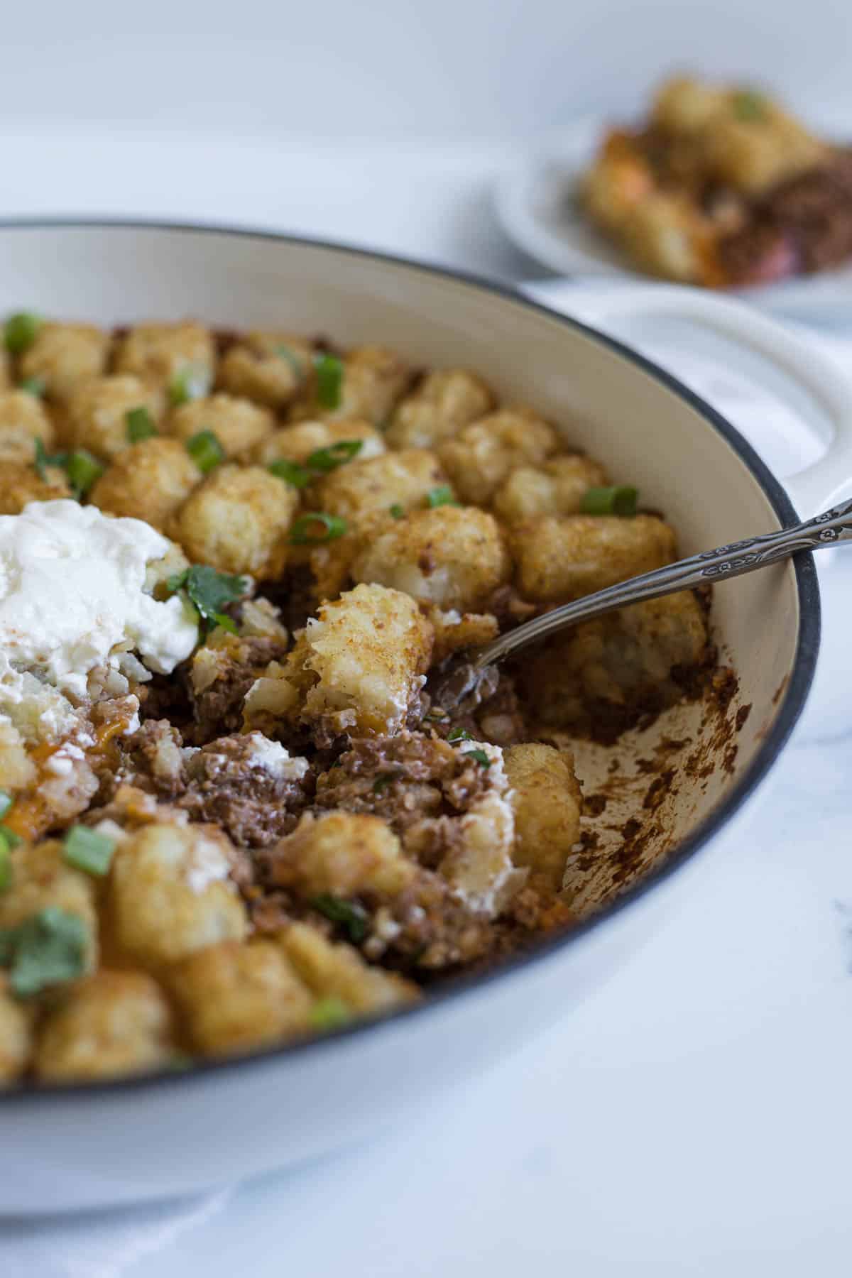 A side view of the tater tot casserole in a white braiser.