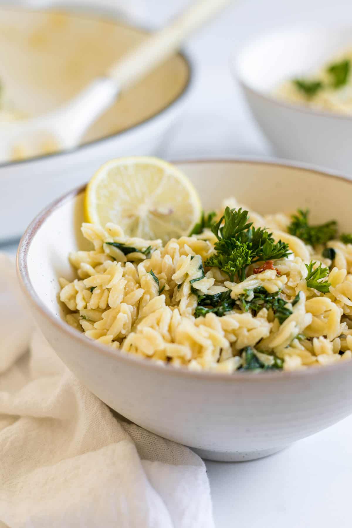 Orzo With Spinach and Feta is in a bowl with a lemon slice on it.