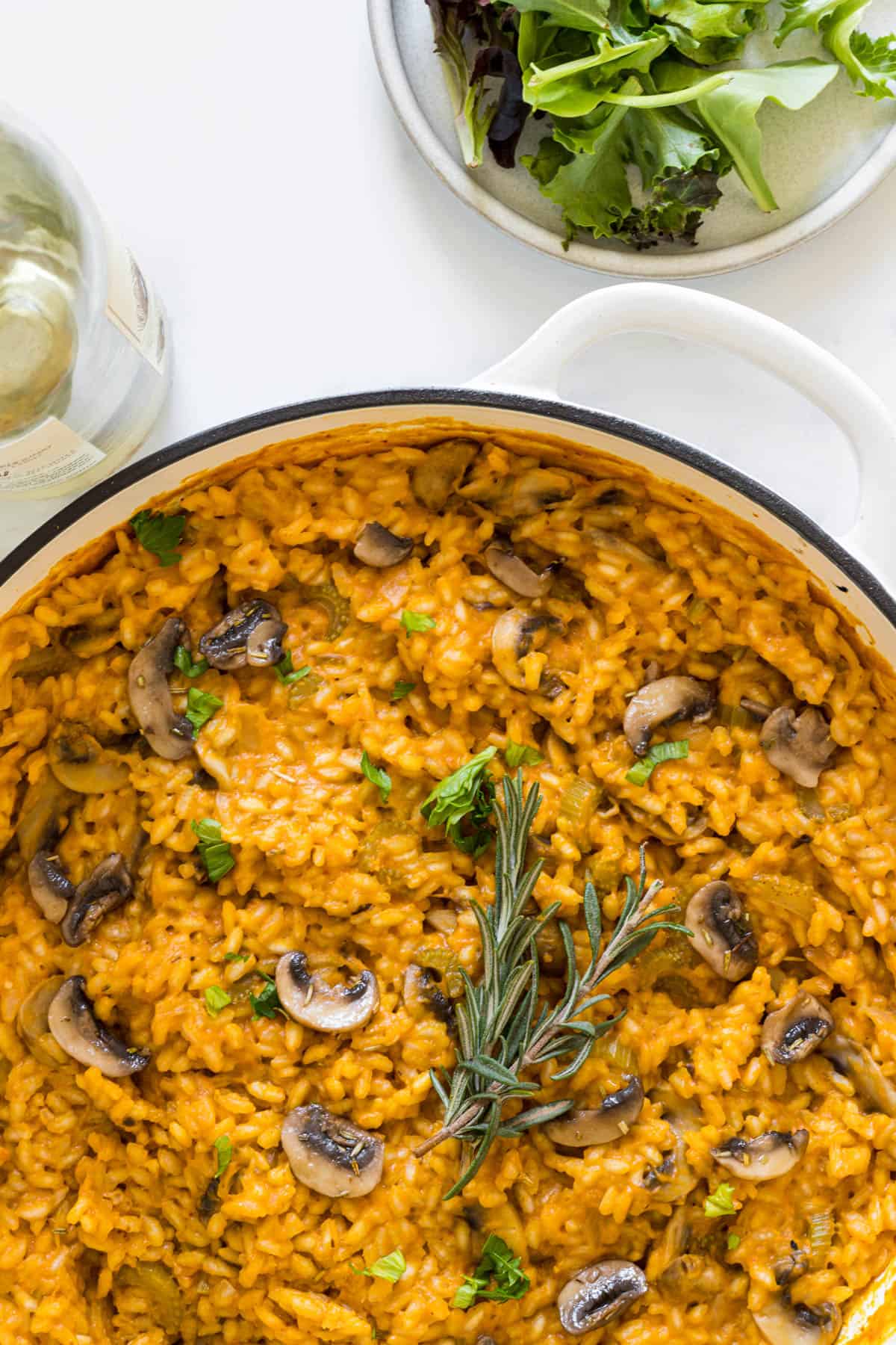 Overhead view of Pumpkin and Mushroom Risotto in a braiser with a white wine bottle and a plate of salad next to it.