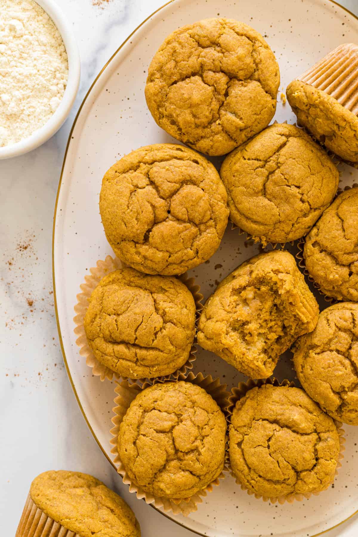 Overhead view of a plate of Gluten-Free Pumpkin Banana Muffins. One muffin has a bite out of it.