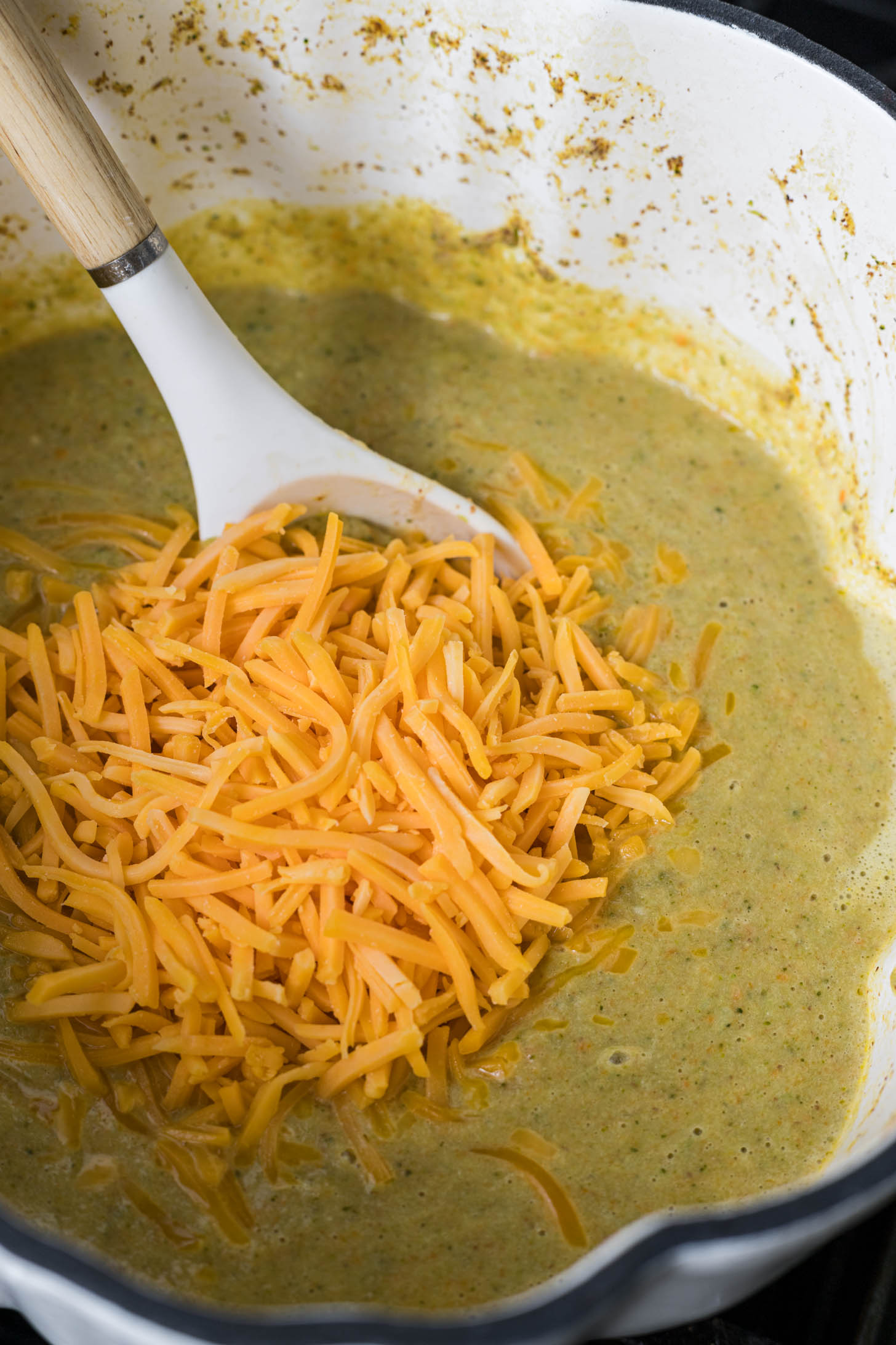 The soup is creamy and has shredded cheese poured on top that is about to get mixed into the soup.