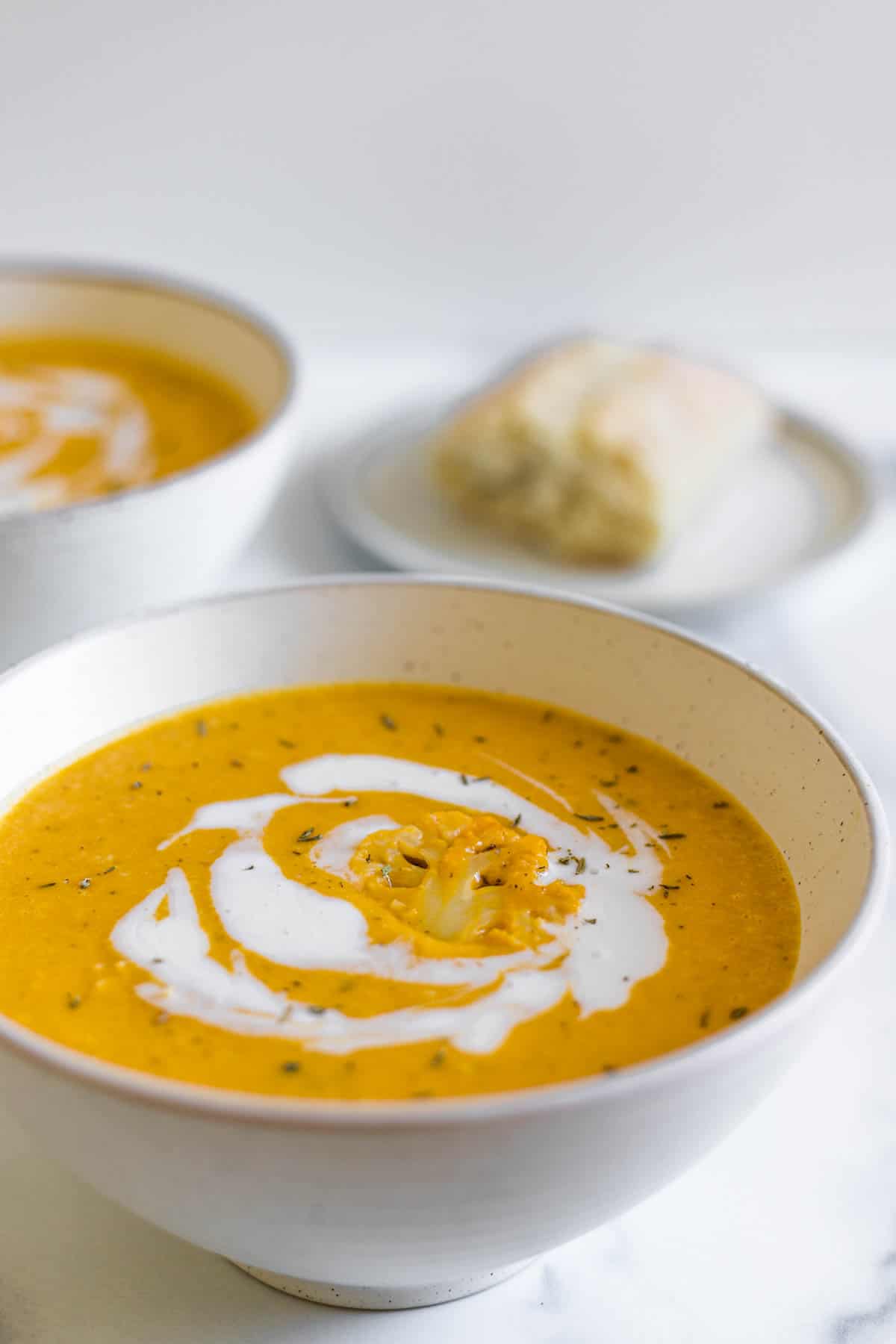 A bowl of pumpkin soup with bread in the background.