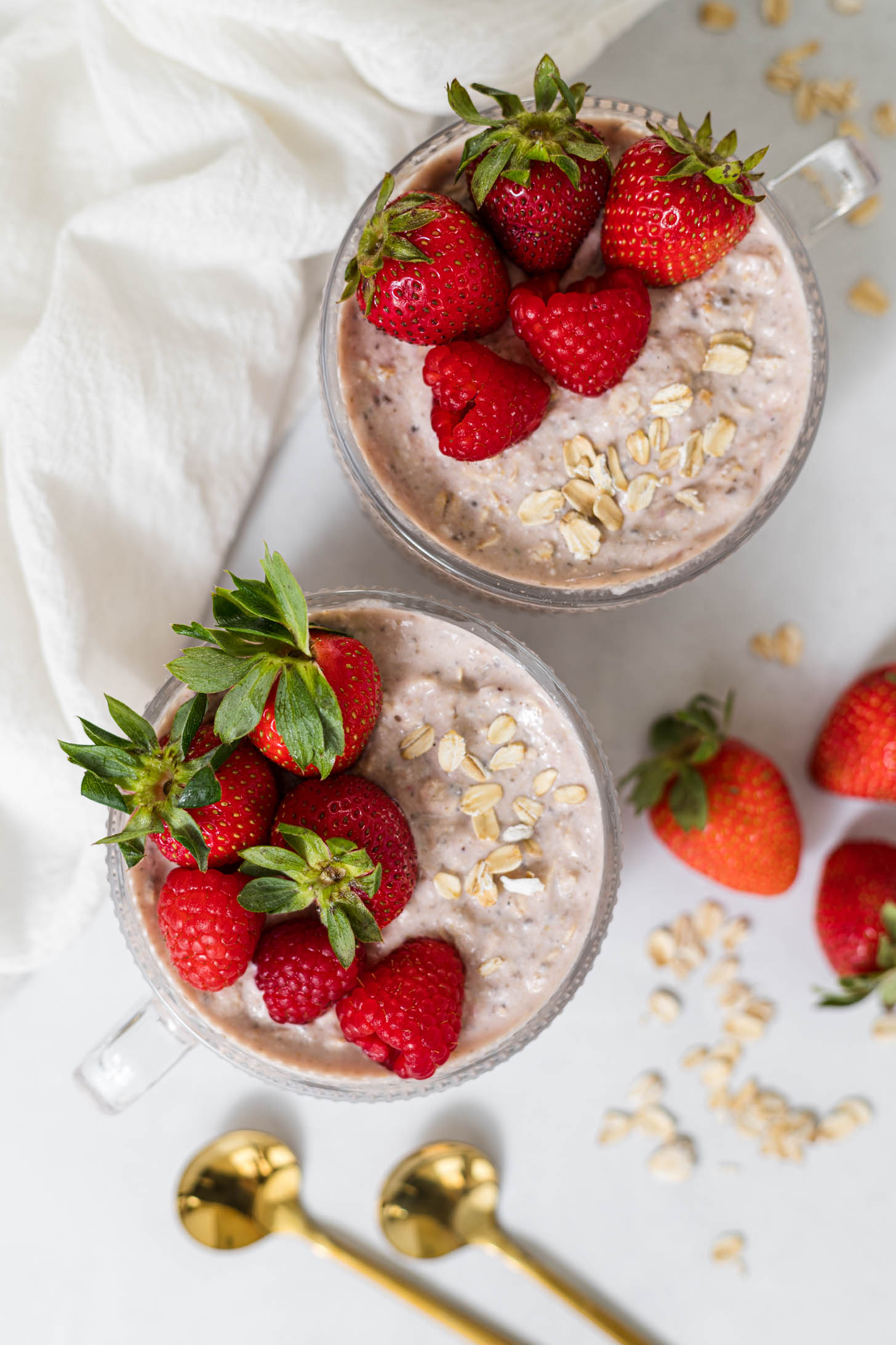 Two cups of overnight oats that are topped with strawberries and raspberries.