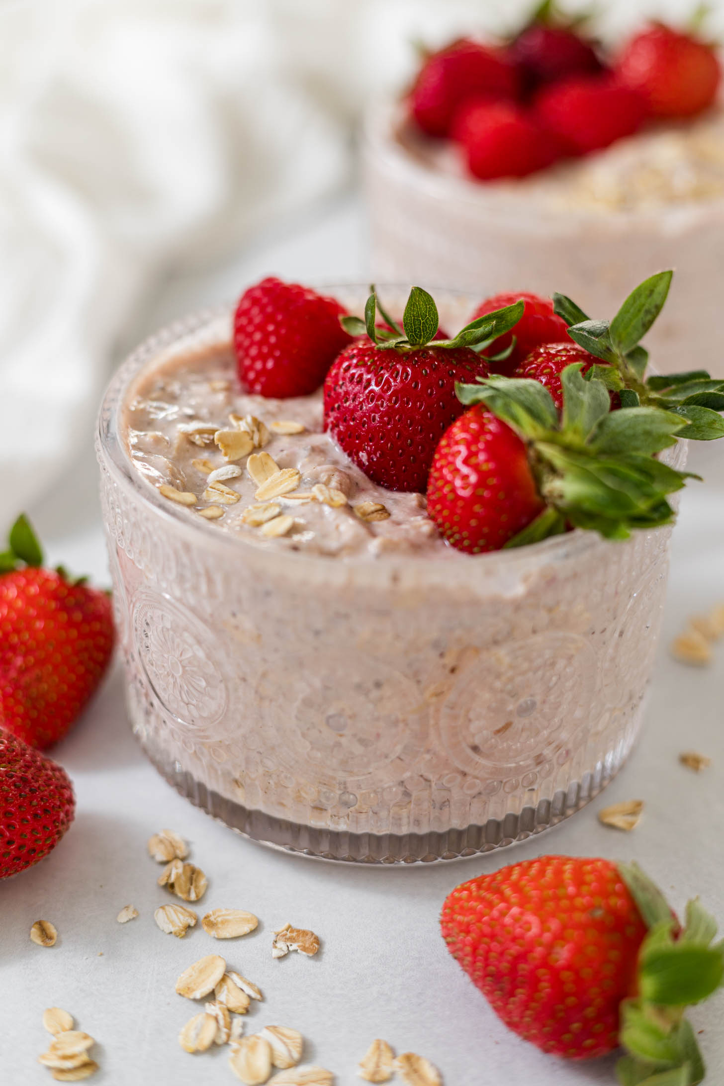 Berry Cheesecake Overnight Oats in a glass cup with strawberries on top.