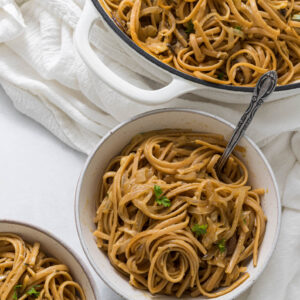 Overhead view of two bowls of one pot french onion pasta, with a braiser full of pasta sitting to the side of the bowls.