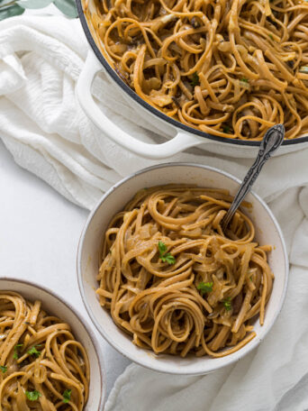 Overhead view of two bowls of one pot french onion pasta, with a braiser full of pasta sitting to the side of the bowls.