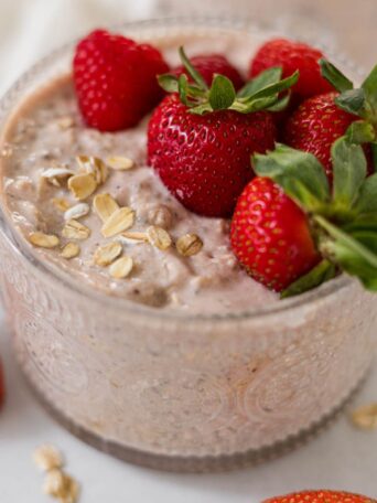 Berry Cheesecake Overnight Oats in a glass cup with strawberries on top.