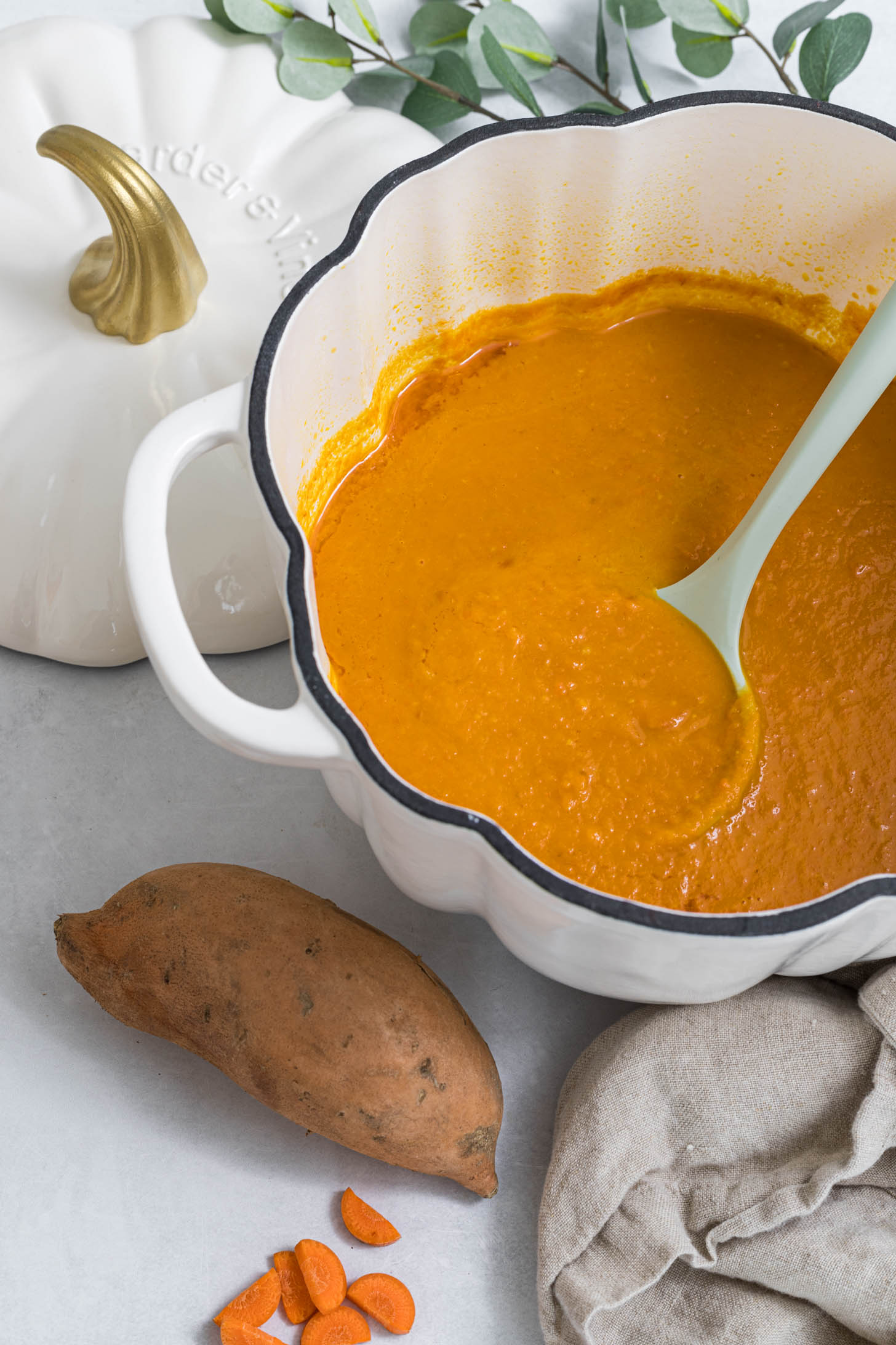 Prepared soup with a serving spoon in it and a sweet potato is laying next to it.