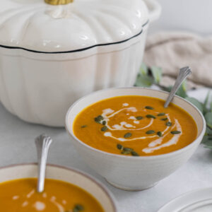 Two bowls of Carrot Ginger Sweet Potato Soup with a Pumpkin Dutch Oven behind them.