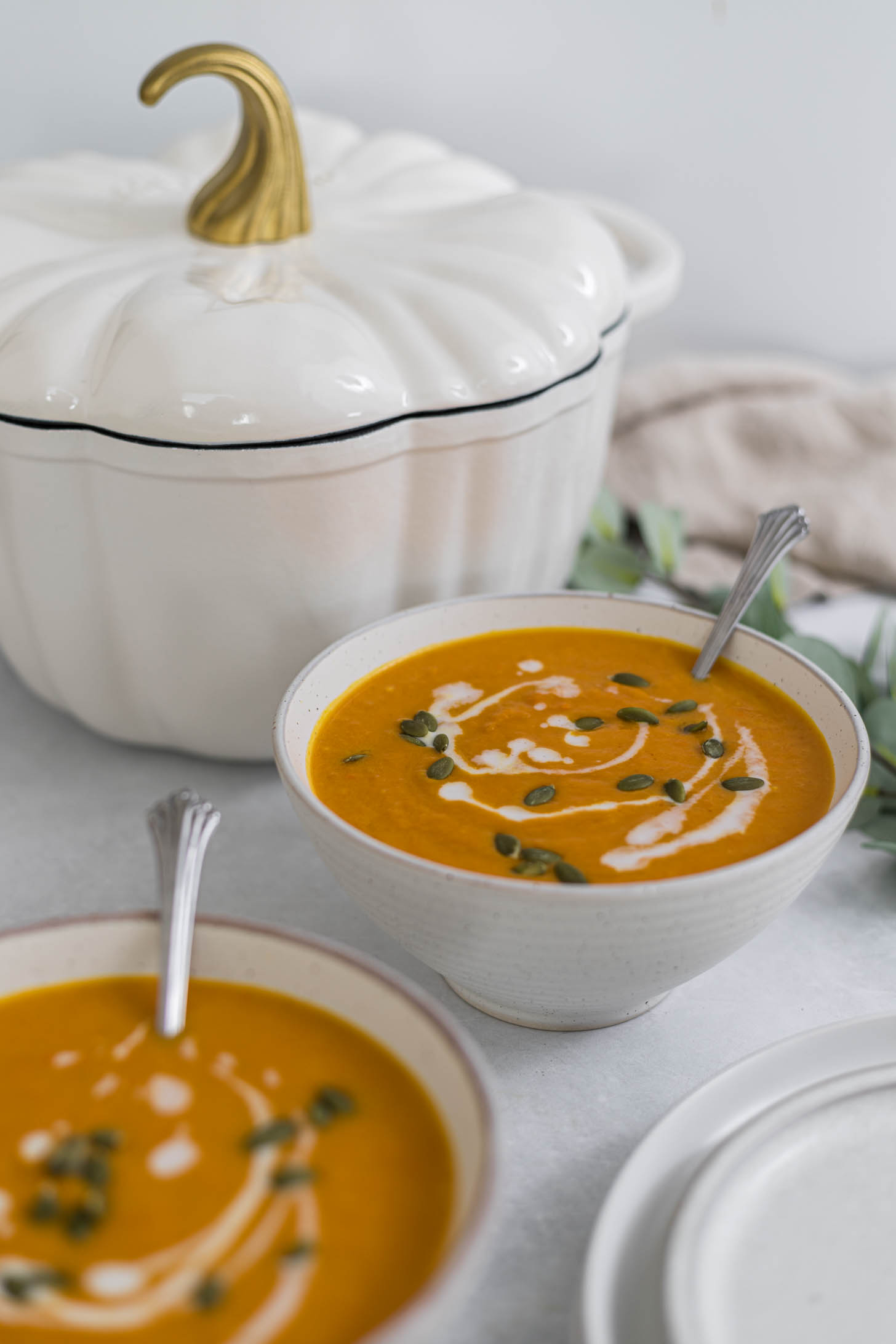 Two bowls of Carrot Ginger Sweet Potato Soup with a Pumpkin Dutch Oven behind them.