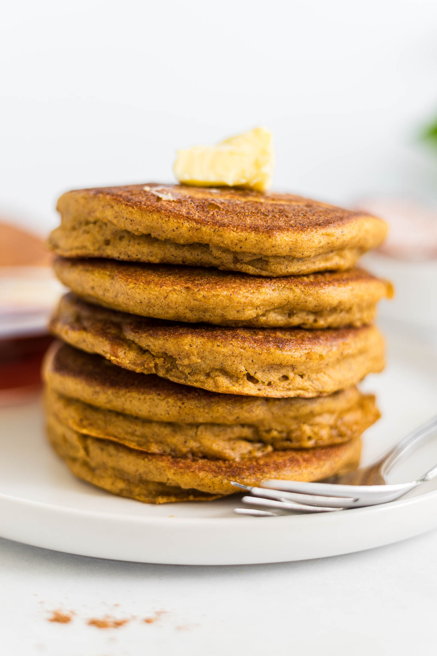 A stack of gluten-free pumpkin pancakes with a dollop of butter on top.